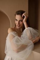 Portrait of a beautiful bride in full growth in the studio on a white background. The woman stands with her back and looks into the frame. photo