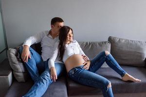 A man and a pregnant woman are sitting hugging on the couch. photo