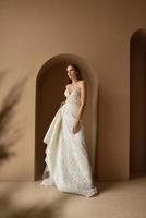 Portrait of a beautiful bride in full growth in the studio on a white background. The woman stands with her back and looks into the frame. photo