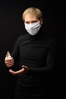 A portrait of man with medical face mask using disinfectant spray on hands. People, medicine and healthcare concept. Coronavirus protection photo