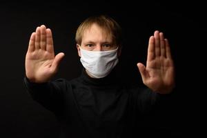 Middle-aged man in a medical mask shows a stop with his hand. The concept of protection against coranavirus. photo