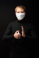un retrato de un hombre con mascarilla médica usando spray desinfectante en las manos. concepto de personas, medicina y atención médica. protección contra el coronavirus foto