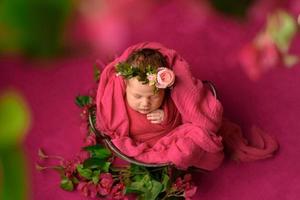 Closeup portrait of cute newborn girl sleeping wrapped in purple soft blanket, wearing stylish head flower, baby fashion concept