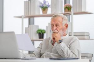 un anciano preocupado revisando sus facturas, una familia anciana jubilada leyendo documentos, un hombre maduro en la sala de estar con una laptop foto