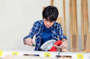 Young carpenter using a screwdriver fixing circular saw in carpentry workshop, Child learning woodworking in the craftsman workshop photo