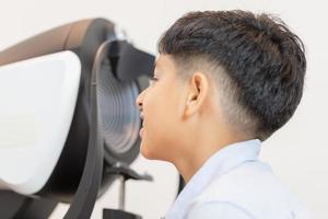 Indian boy doing eye test checking examination with autorefractor in optical shop photo