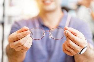 Cheerful man holding eyeglasses in optics store, happy man choosing glasses at optics shop photo