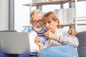 retrato de una feliz pareja mayor comprando en línea en la sala de estar, una anciana y un hombre usando una computadora portátil en un acogedor sofá en casa, conceptos familiares felices foto