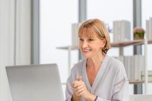 Portrait of woman using laptop and smartphone at home, Mature woman in living room with laptop talking video call on modern computer gadget photo