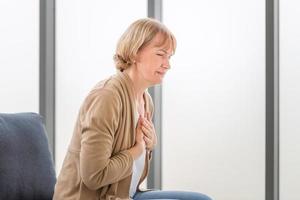 anciana con dolor en el corazón en la sala de estar, la mujer madura presiona la mano contra el pecho tiene un ataque al corazón sufre un dolor insoportable foto