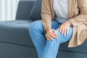 Woman suffering from knee pain sitting sofa in the living room, Mature woman suffering from knee pain while sitting on the sofa photo