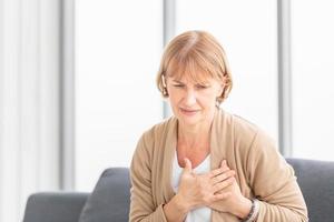 anciana con dolor en el corazón en la sala de estar, la mujer madura presiona la mano contra el pecho tiene un ataque al corazón sufre un dolor insoportable foto