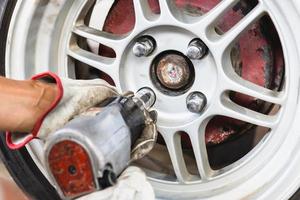 Close up of repair mechanic hands during maintenance work to pneumatic gun to loosen a wheel nut changing tyre of car photo