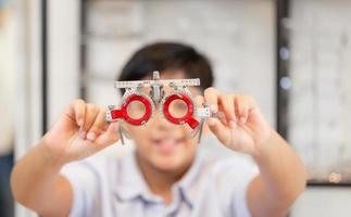 niño indio con marco de prueba de optometrista en clínica oftalmológica, niño haciendo examen de control de prueba ocular con optometrista usando marco de prueba en tienda óptica foto