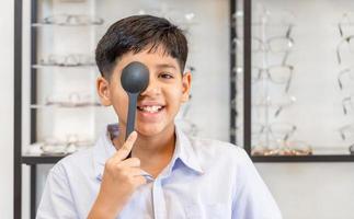 retrato de niño revisando la visión en la clínica de oftalmología, niño indio-thai sonriente eligiendo anteojos en la tienda de óptica, examen ocular en la tienda de óptica