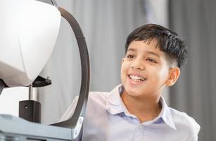 niño indio haciendo examen ocular con autorefractor en una tienda óptica, optometrista haciendo pruebas visuales para pacientes infantiles foto