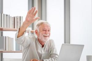 Portrait of senior man using laptop using laptop talking on video call at home, Happy senior man in living room with laptop computer gadget photo