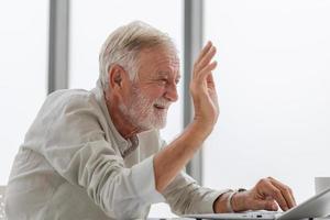Portrait of senior man using laptop using laptop talking on video call at home, Happy senior man in living room with laptop computer gadget photo