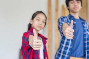 Kids standing with giving thumbs up as a sign of success in a carpentry workshop photo
