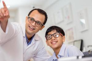 niño haciendo un examen ocular con un optometrista en una tienda de óptica, un niño indio-thai sonriente eligiendo anteojos en una tienda de óptica foto