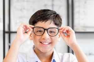 niño indio-thai sonriente eligiendo anteojos en la tienda de óptica, retrato de un niño de raza mixta que usa anteojos en la tienda de óptica foto