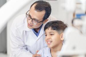 Boy doing eye test checking examination with optometrist in optical shop, Smiling Indian-thai boy choosing glasses in optics store photo