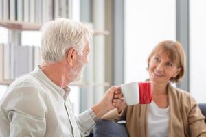 Senior man and woman holding cups of coffee in living room, Senior couple inside home during a coffee break photo
