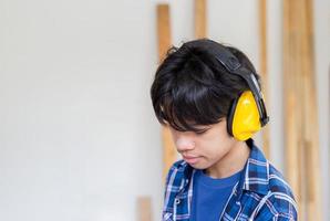 Young boy standing with noise reduction earmuffs in a carpentry workshop. Kid learning in the craftsman workshop