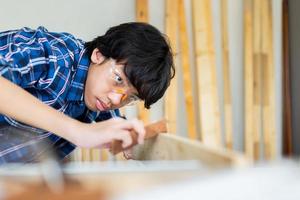 joven carpintero trabajando en carpintería en taller de carpintería, carpintero trabaja la madera con papel de lija foto