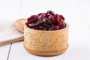 Dried cranberries in a wooden cup with a lid and burlap on a white wooden table photo