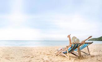 Young asian woman relaxing on beach chair arm up her hand with floppy hat photo