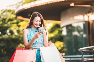 mujer asiática sostiene una bolsa roja y usa un teléfono inteligente foto