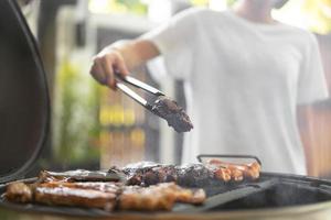 Woman hand grilling barbecue on fire at backyard on day photo