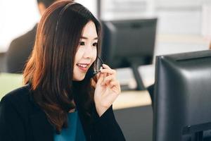 mujer asiática del personal de negocios joven que trabaja con auriculares y computadora para obtener apoyo. foto