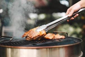 Man hand grilling barbecue with smoked at backyard on day photo