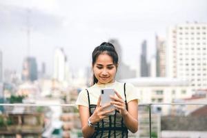 joven mujer asiática adulta de negocios que usa el teléfono móvil para el texto de la aplicación de citas en línea y el chat desenfoque de fondo de la ciudad. foto