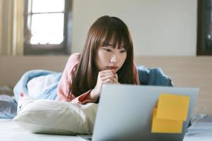 Asian teenager woman in bedroom and use computer for work and study in morning on weekend. photo