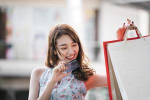 hermosa sonrisa joven mujer asiática mostrar tarjeta de crédito con bolsas de compras. foto