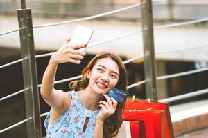 selfie de mujer asiática con bolsas rojas y tarjeta de crédito