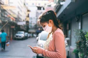 Asian adult woman tan skin wear mask on face and using smartphone. photo