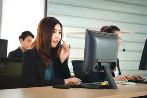 Positive look young business staff asian woman using headphone and computer for support. photo
