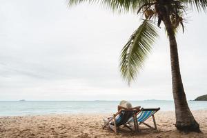 mujer asiática en silla de playa bajo palmera tropical foto
