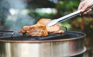 Man hand grilling barbecue on fire at backyard on day photo