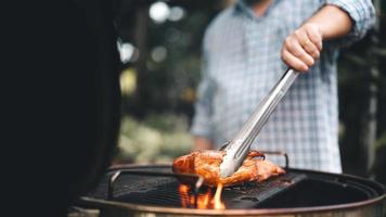 Man hand grilling barbecue on fire at backyard on day photo