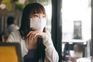 Young adult asian female with protective face mask for virus covid 19 work and study at cafe on day. photo