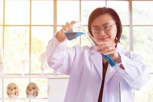 descubriendo una cura para una científica asiática que está concentrada, sosteniendo un tubo de ensayo y observando mientras trabaja. foto