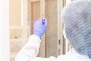 An Asian female scientist is writing down the formula for calculating chemistry on clear glass in a lab. photo