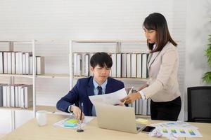 An Asian female supervisor stands with a young male employee on her desk with a serious face.