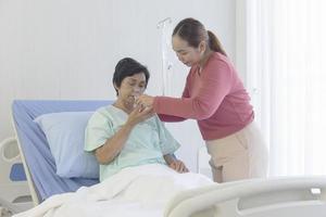 An Asian woman is taking care of her sick mother in a hospital bed. photo