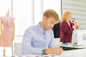 Diseñadores de trabajo en equipo profesional, hombres jóvenes y mujeres mayores en la oficina con una variedad de tonos de tela y equipos para varios diseños. foto